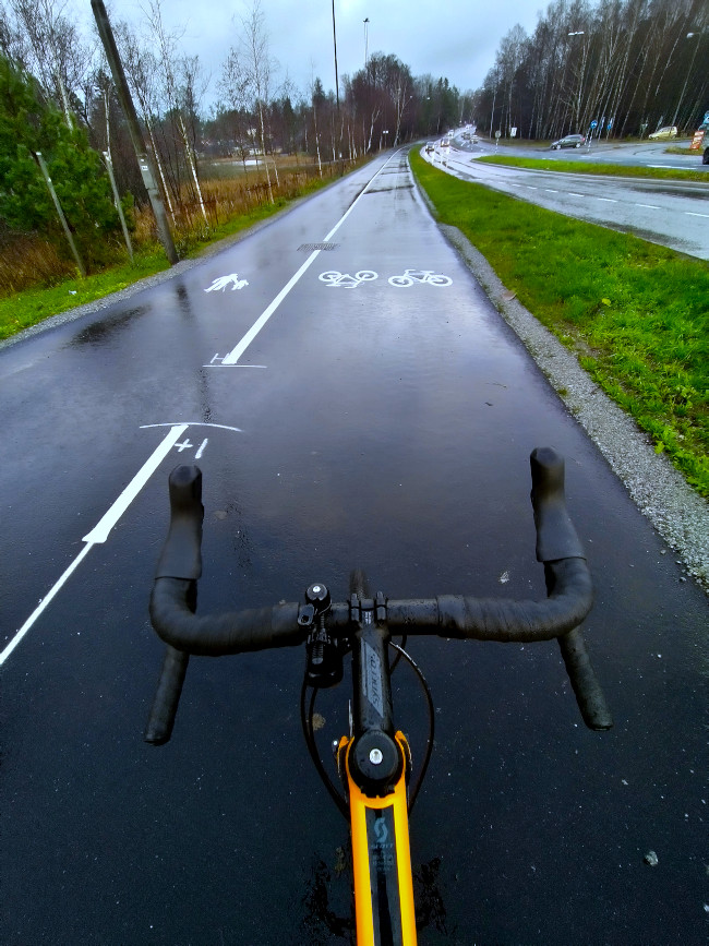 Cykelstyre i förgrunden vid en gång- och cykelväg jämte bilväg