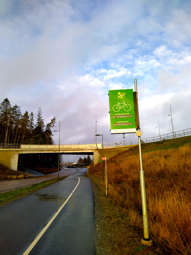 En grön skylt som räknar cyklister framför blå himmel